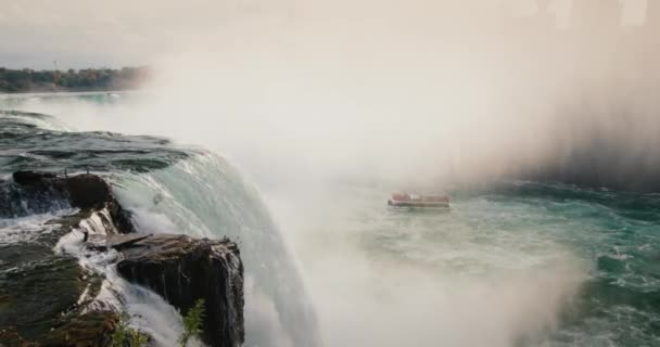 著名的尼亚加拉瀑布是纽约州和美国的一个地标。在河的远方，有一艘载着游客的船在漂流 — 图库视频影像