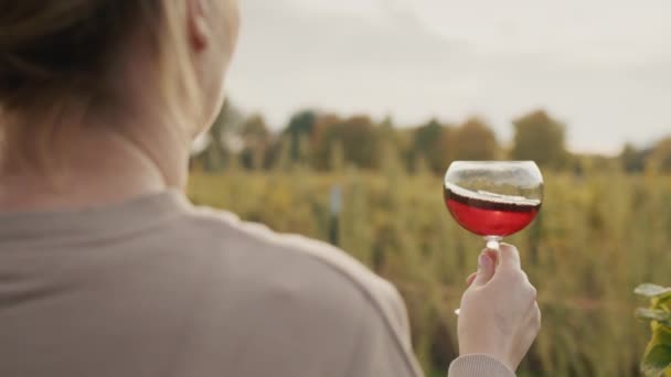 Una mujer con una copa de vino tinto se encuentra cerca de un viñedo. Degustación y tour del vino — Vídeo de stock