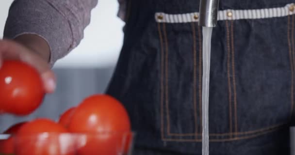 Una mujer tiene las manos bajo un chorro de agua del grifo. Lavar los tomates maduros — Vídeo de stock