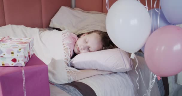 Ein Kind schläft in seinem Bett neben Geschenkboxen und Luftballons. — Stockvideo