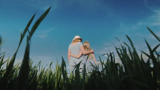 Bajo ángulo de tiro: Mamá abraza a la hija, de pie en un hermoso prado verde contra un cielo azul claro — Vídeos de Stock