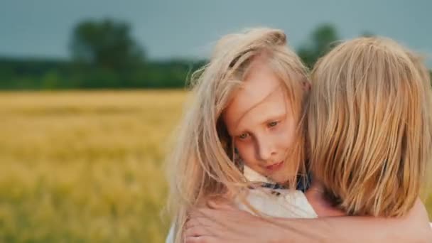 Anya megöleli a lányát naplementekor, a szél játszik a hajukkal. — Stock videók