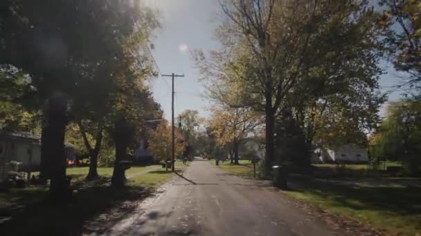 Przejazd typową ulicą amerykańskiego miasta w pogodny jesienny dzień. Słońce pięknie oświetla domy i drzewa. 4k strzał — Wideo stockowe