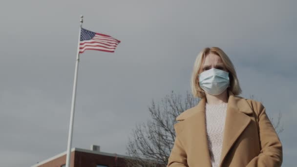 Portret van een vrouw met een beschermend masker tegen de achtergrond van een gebouw met een Amerikaanse vlag — Stockvideo