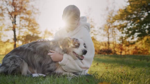 A ten-year-old girl is stroking her dog, sitting in the park on the grass. Walking with your beloved pet — Stok video