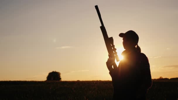 Silueta ženy s odstřelovací puškou. Stojí v paprscích zapadajícího slunce — Stock video