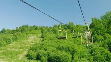 Teleferik koltuk. Yukarı doğru bir ormanla kaplı bir orman arka planı hareket ediyorlar. Dağlarda tatil yaz