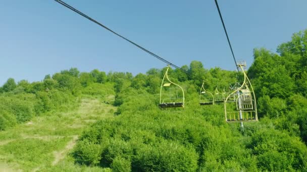 Sedili dell'impianto di risalita. Si muovono verso l'alto sullo sfondo di una foresta coperta da una foresta. Vacanze in montagna in estate — Video Stock