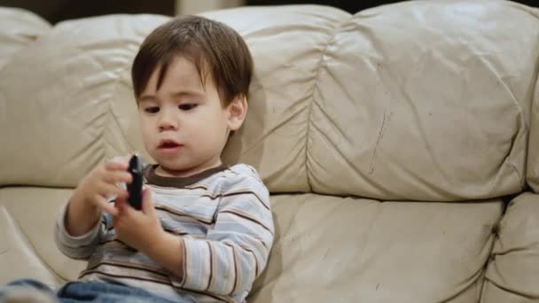 Asian two years old kid watches TV, holds a remote control in his hands — 비디오