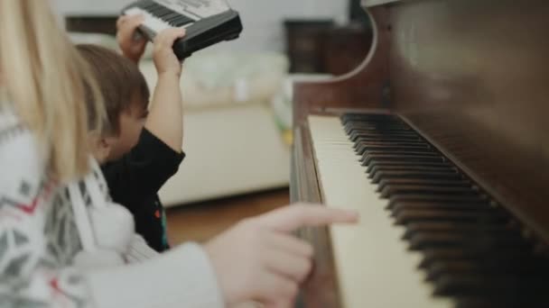 Children are in together, playing the piano. The kid brings his piano and plays with his sister. — Stock video