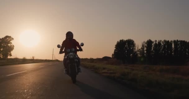 Silueta unui motociclist pe o motocicletă, merge pe autostradă în razele apusului de soare — Videoclip de stoc