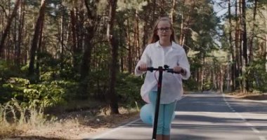 Çocuk scooter kullanıyor, balonlar arkadan bağlanıyor.