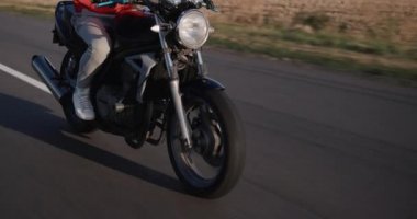 Bir motosikletçi mısır tarlaları boyunca kırsal bir yolda gidiyor..