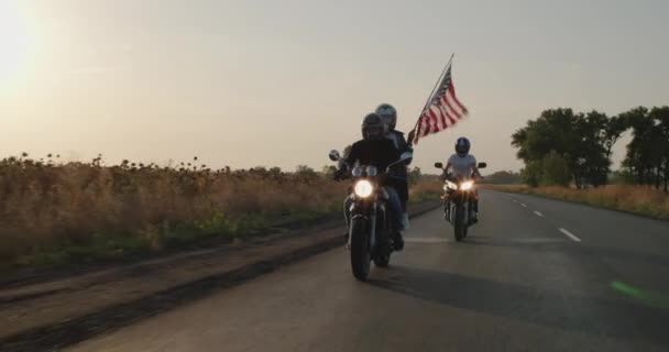 A group of young men rides motorcycles at sunset, followed by the U.S. flag — стоковое видео