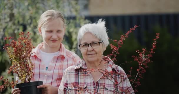Retrato de una anciana con su nieta sosteniendo macetas para plantar en el jardín — Vídeo de stock