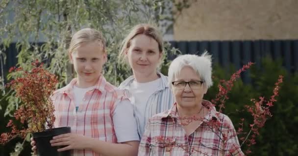 Portrait of mother, daughter and granddaughter - together in their garden, holding flower pots for planting — Stockvideo