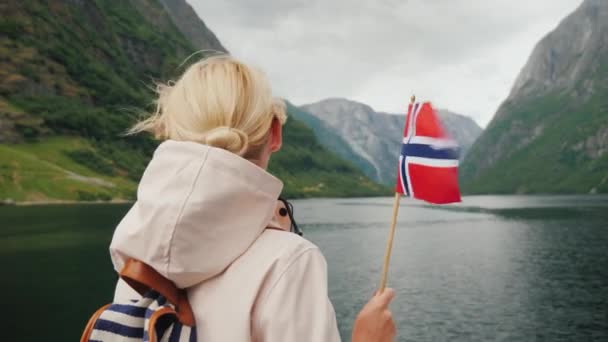 Uma pessoa com uma bandeira norueguesa em suas mãos viaja em um navio em um fiorde pitoresco — Vídeo de Stock