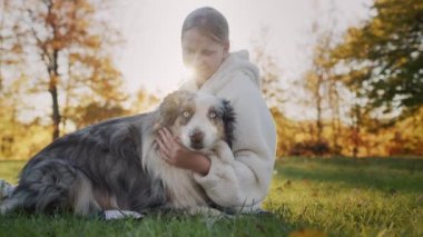 A ten-year-old girl is stroking her dog, sitting in the park on the grass. Walking with your beloved pet. 4k video