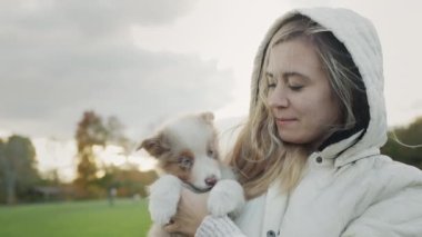 The owner of the puppy holds the pet in his arms. Walking together in the autumn park.