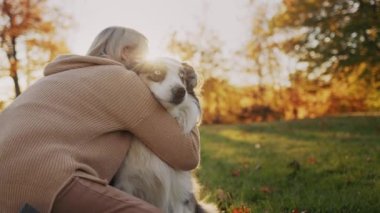 A woman gently hugs her beloved dog. On a walk in the park, the sun illuminates them beautifully.