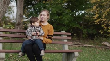 A young mother with a little son sits on a bench in the park.