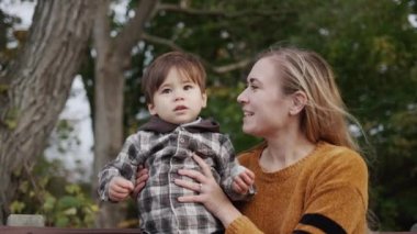 A young mother with a little son sits on a bench in the park.