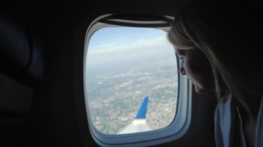 A young female passenger looks out of the window of the plane to the ground far below, where the metropolis is visible.
