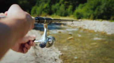 A man is fishing in a small mountain river, catches a carnivorous fish by spinning a spoon-baitr.
