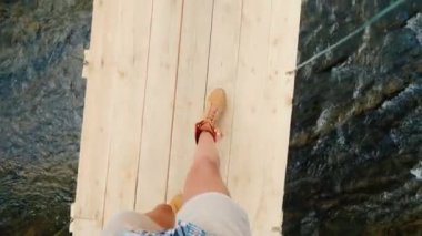 Trekking botları bir adam uçurumun üzerinde bir ahşap köprü kenarı boyunca girer. POV video