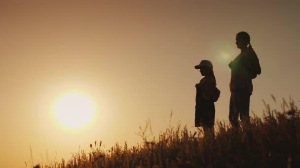 一个女人和一个孩子的剪影 他们背着背包站在后面 欣赏日落 一起旅行概念 — 图库视频影像
