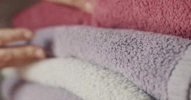 Womens fingers sort through clean towels on a shelf in the closet.