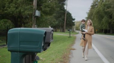 A woman with a boy in her arms goes to the mailbox to send a letter