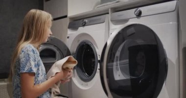 A teenage girl transfers clean clothes from the washing machine to the dryer.