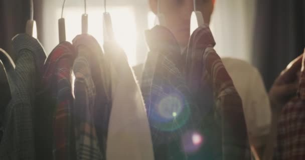 Young Man Chooses Shirt Dressing Room Shop Sun Window Illuminates — стоковое видео