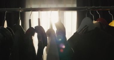 Rack with hangers with clothes in the rays of the setting sun that shines from the window.