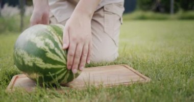 Woman cutting a piece of watermelon at a picnic.