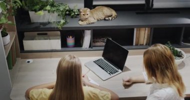 Teacher or parent helping a girl who is working with a laptop in the classroom.