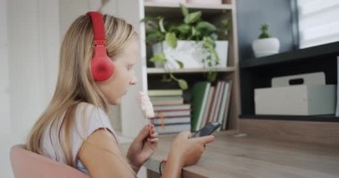 A teenager in headphones uses a smartphone, eats ice cream in his room.