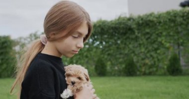 Cute little girl sitting in the park with a puppy in her arms.