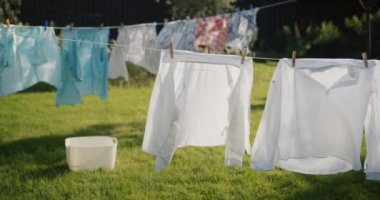 Evin arka bahçesinde giysiler ve yataklar kuruyor, yakınlardaki çimlerin üzerinde bir çamaşır sepeti duruyor.