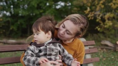 A young mother with a little son sits on a bench in the park.