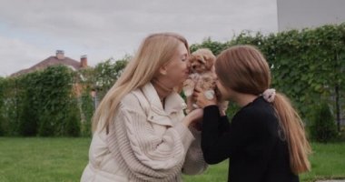 Anne ve kızı evin arka bahçesinde küçük bir köpekle oynuyorlar..