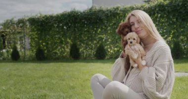 Kollarında köpek yavruları olan hamile bir kadının portresi. Evinin arka bahçesindeki çimlerde oturuyor..