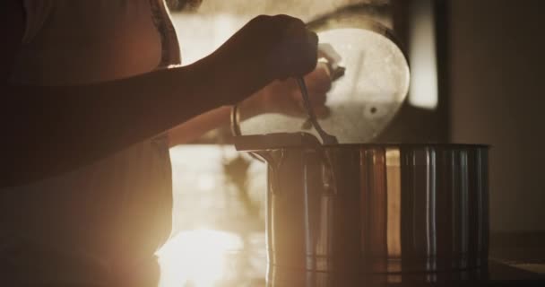 一位家庭主妇正在厨房的锅子里煮汤 夕阳西下的阳光从窗户射了出来 — 图库视频影像