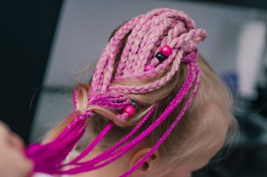 Pembe saç örgüleri, sarışın bir kızın üzerinde. 5 yaşında, kapalı mekanda çekilmiş.