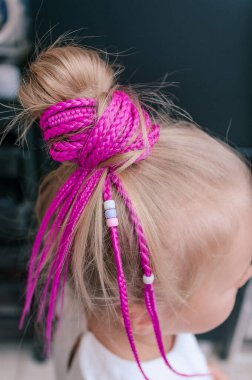 Pembe saç örgüleri, sarışın bir kızın üzerinde. 5 yaşında, kapalı mekanda çekilmiş.