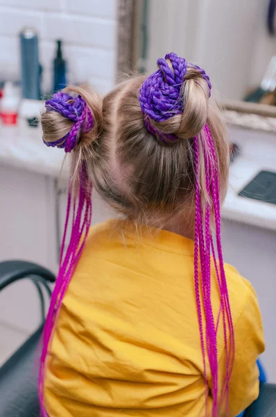 一个5岁的金发女孩在室内特写 在淡紫色粉红阴影下的彩色辫子 后视镜 — 图库照片