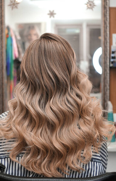 Hollywood curls on a young blonde woman in a beauty salon, view from the back