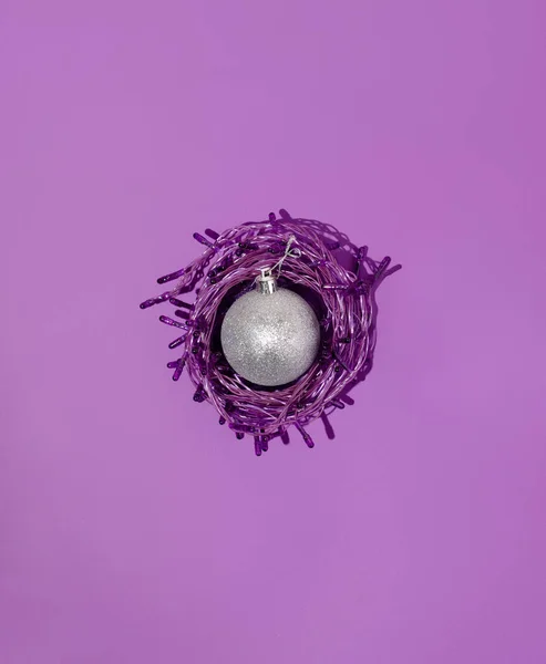 Güzel mor bir arka planda Noel lambalarına sarılı parlak gümüş mücevherli yaratıcı bir konsept. En düşük Yeni Yıl kompozisyonu.