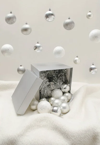 Gümüş ve beyaz Noel ağacı süslemeleri gri hediye kutusuna dökülüyor ve beyaz arka planda aksesuarlar dökülüyor. Yılbaşı hediyesi için yaratıcı kompozisyon.